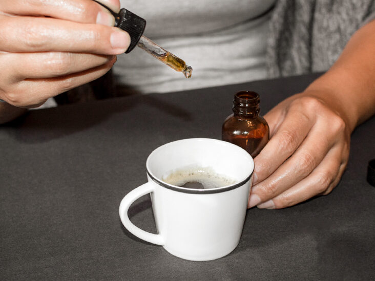 Pouring CBD tincture in a coffee cup, natural medicine made with marihuana. Woman using cannabis oil with a dropper in a table with marihuana bud.